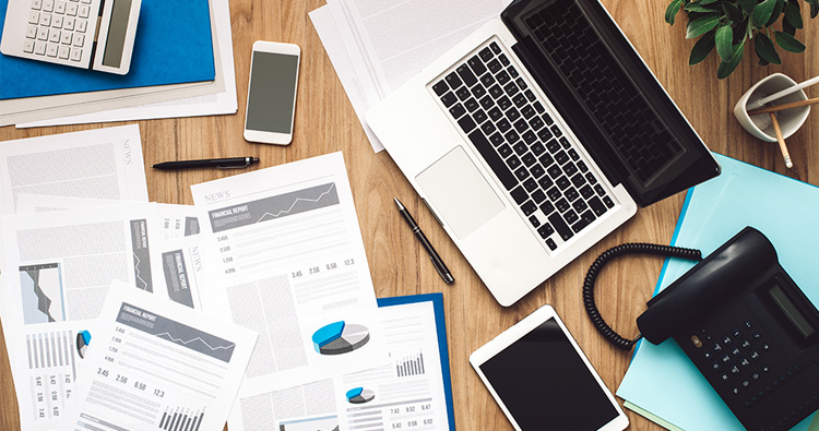 overhead image of a cluttered desk with papers and an open laptop