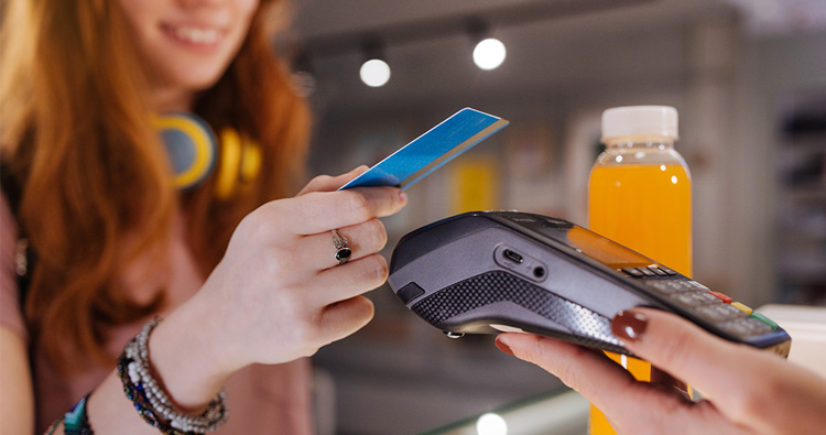 A teenage girl with a credit card in her hand taps it on a portable card reader.